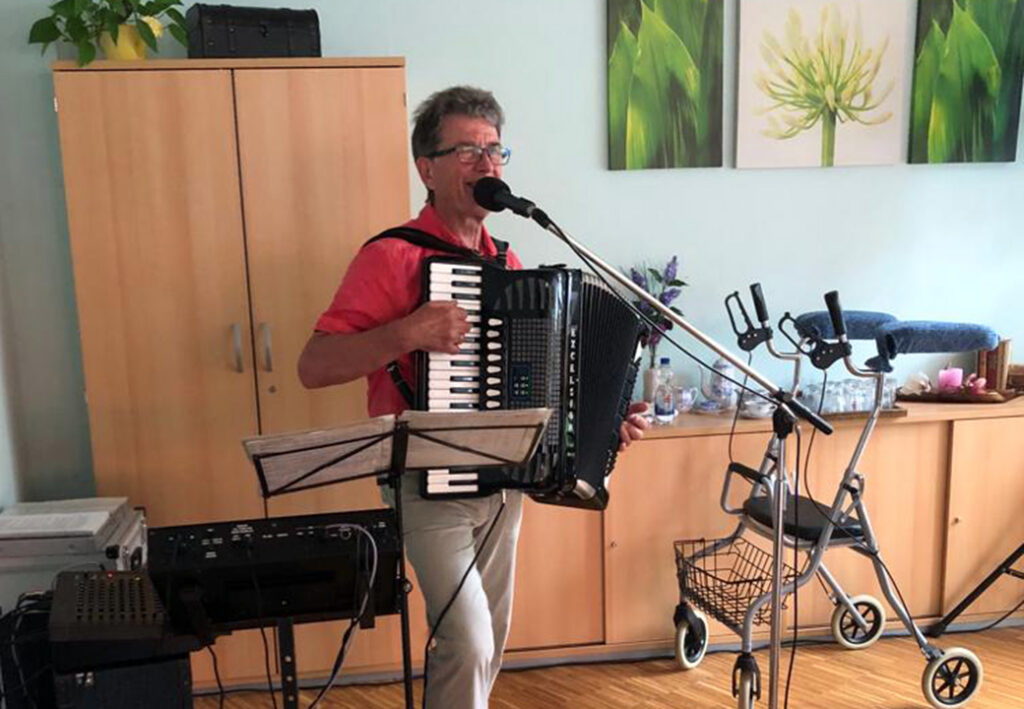 Ein Mann spielt Akkordeon und singt in ein Mikrofon in einem Raum.