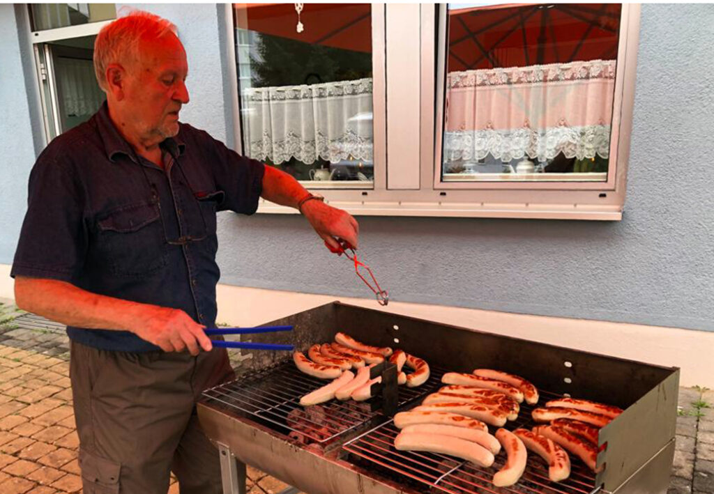 &Auml;lterer Mann grillt W&uuml;rstchen im Freien.