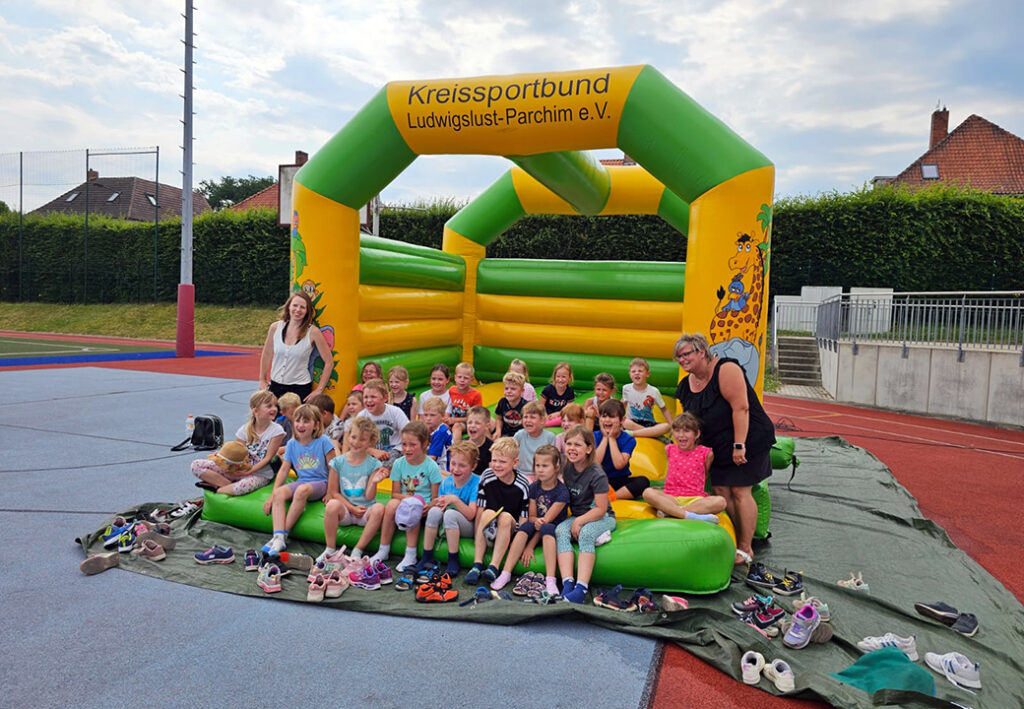 Gruppe von Kindern auf einer Hüpfburg mit zwei Erwachsenen am Rand.