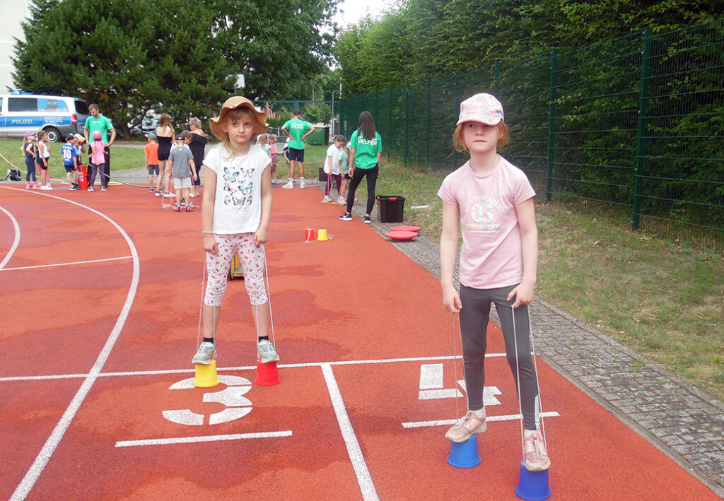 Kinder spielen auf einer Laufbahn mit Stelzenbechern
