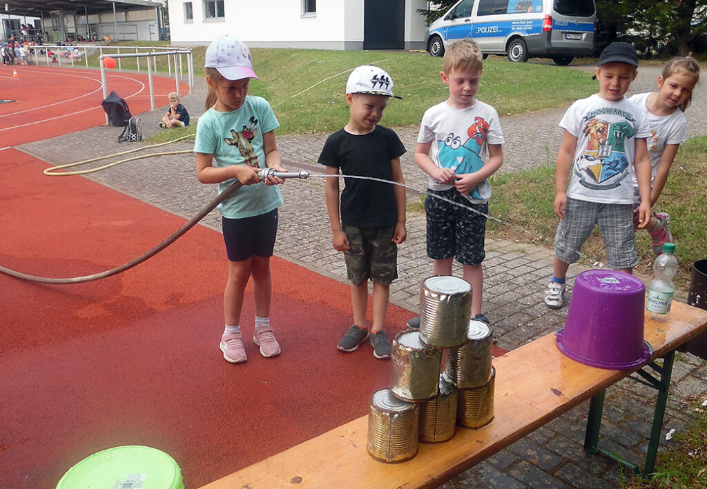 Kinder spielen mit einem Wasserschlauch und Dosen im Freien.