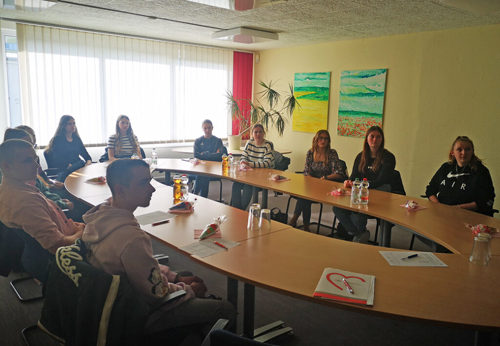 Eine Gruppe von Menschen sitzt an einem U-f&ouml;rmigen Tisch in einem Konferenzraum.