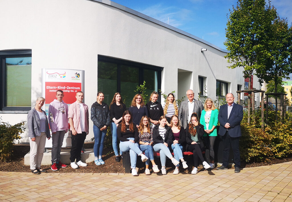 Foto von einer Gruppe von Menschen vor einem Geb&auml;ude mit einem Schild, das Eltern-Kind-Zentrum anzeigt.