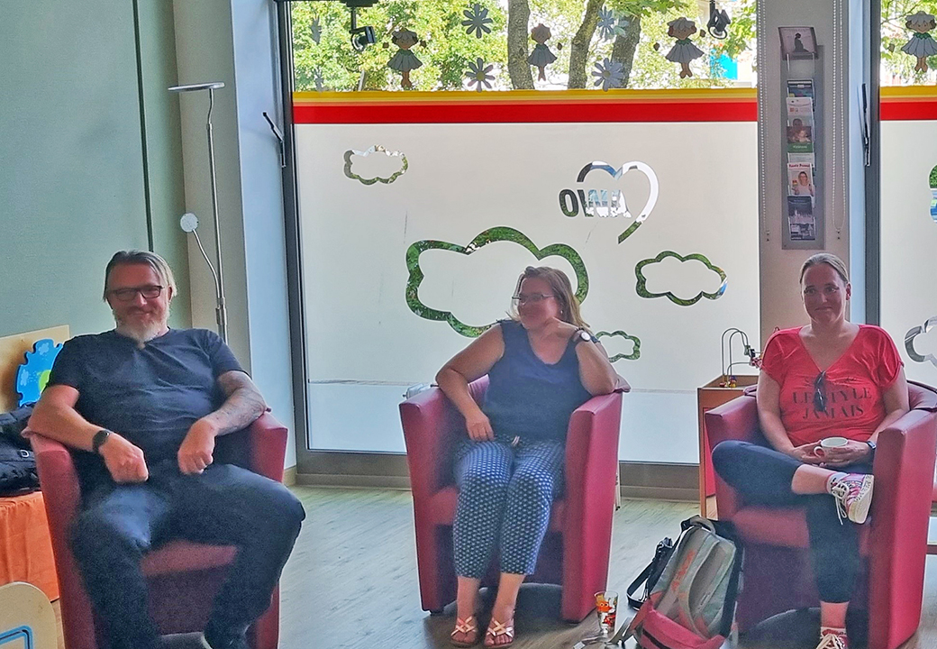 Drei Personen sitzen auf roten Sesseln in einem Raum mit AWO-Dekoration.