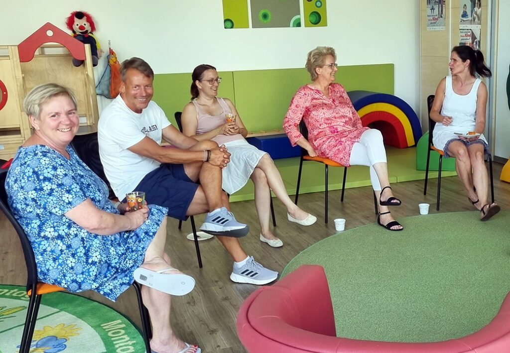 F&uuml;nf Personen sitzen in einem Kreis und unterhalten sich.