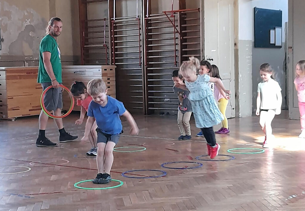 Kinder in einem Turnsaal, die H&uuml;pfspiele mit Reifen spielen.