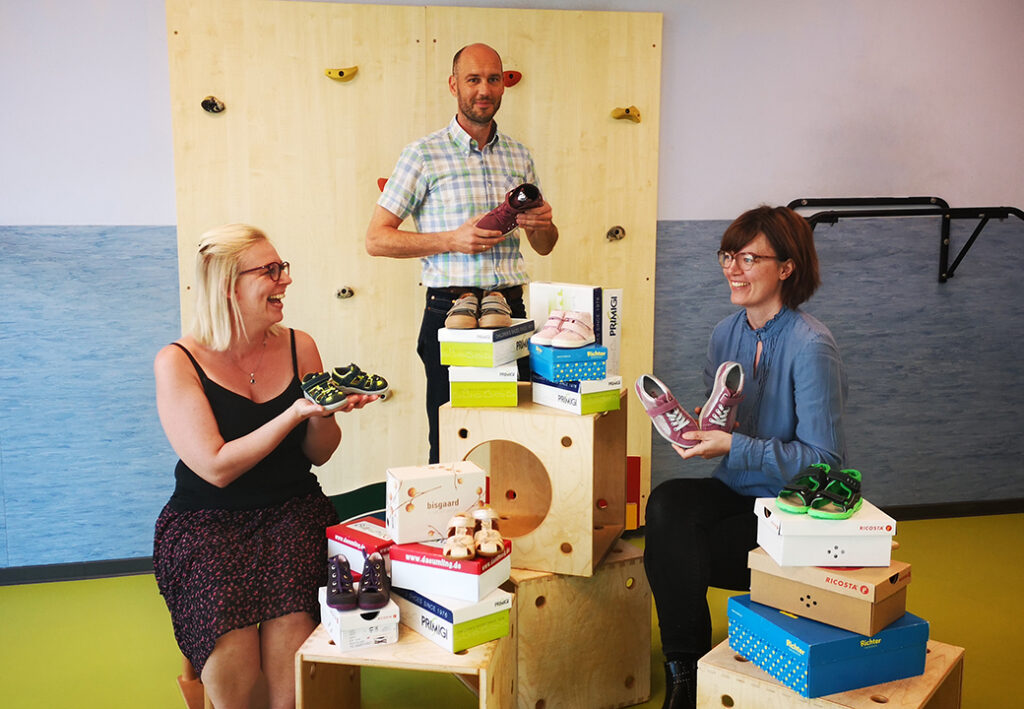 Drei Personen mit Kinderschuhen in einem Raum