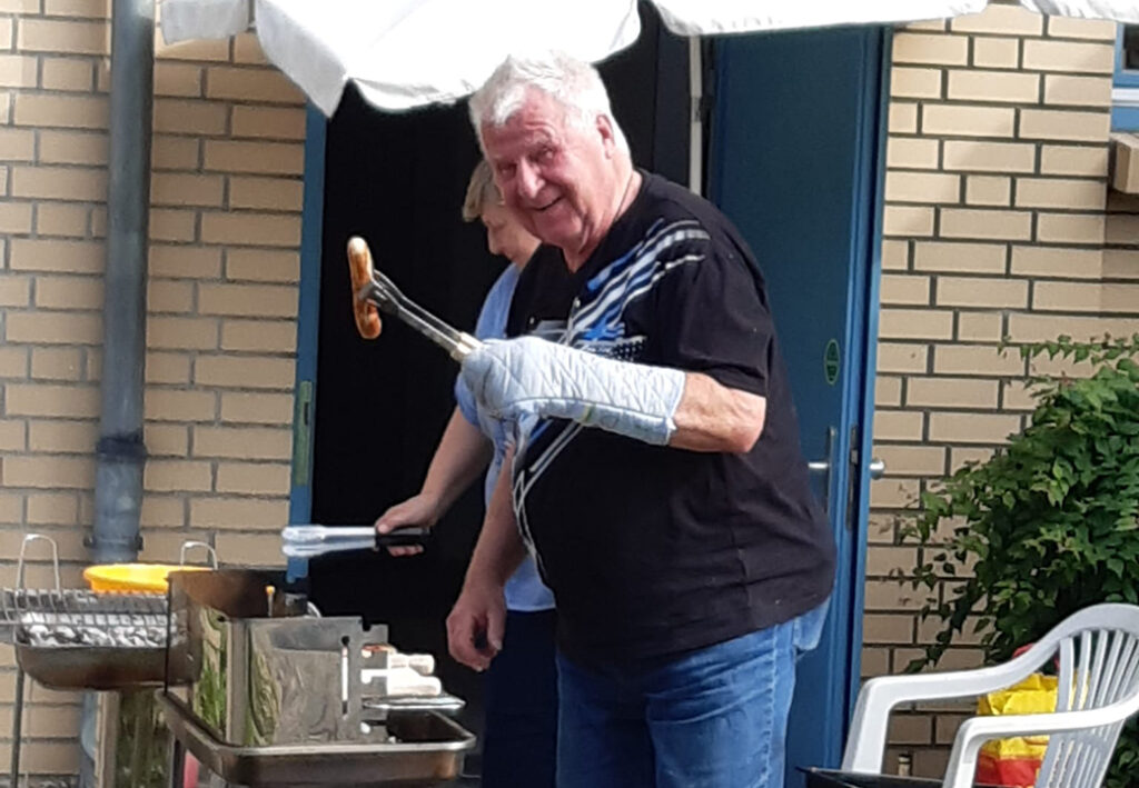 Ein Mann grillt drau&szlig;en eine Wurst vor einem Backsteingeb&auml;ude.