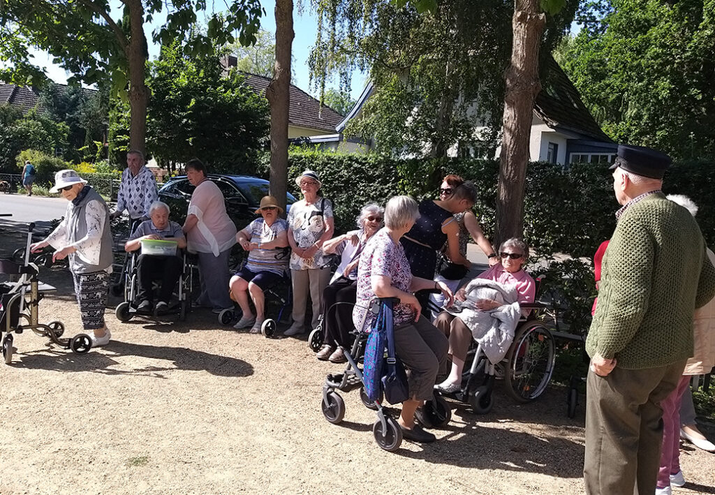 Foto einer Gruppe von Senioren und Betreuern im Freien, viele mit Rollatoren und Rollst&uuml;hlen.