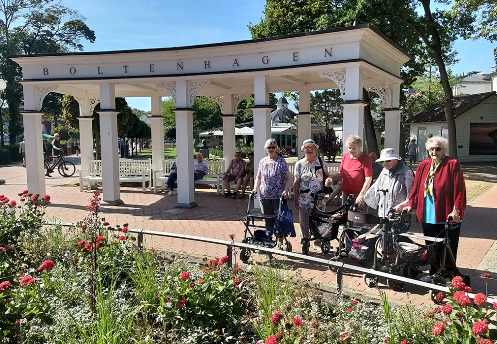 Eine Gruppe &auml;lterer Frauen mit Rollatoren stehen vor einem Pavillon mit der Aufschrift 'Boltenhagen'.
