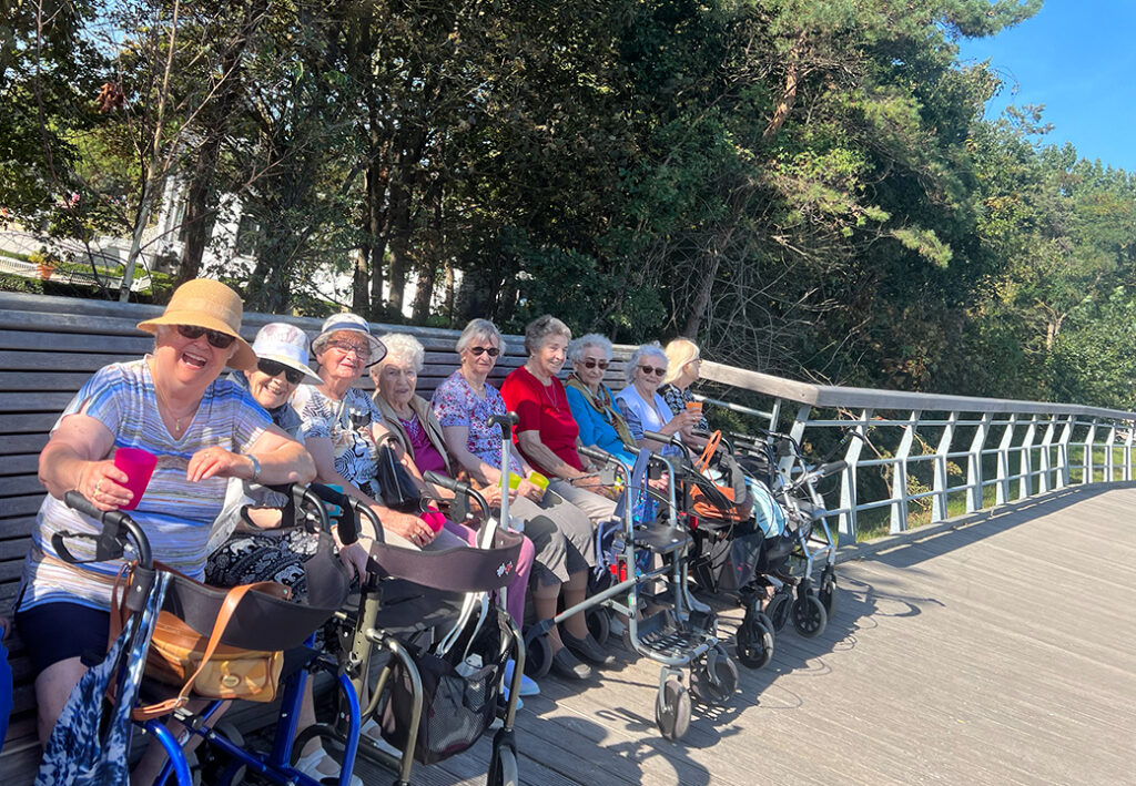 Gruppe von &auml;lteren Frauen mit Rollatoren auf einer Holzbank sitzend
