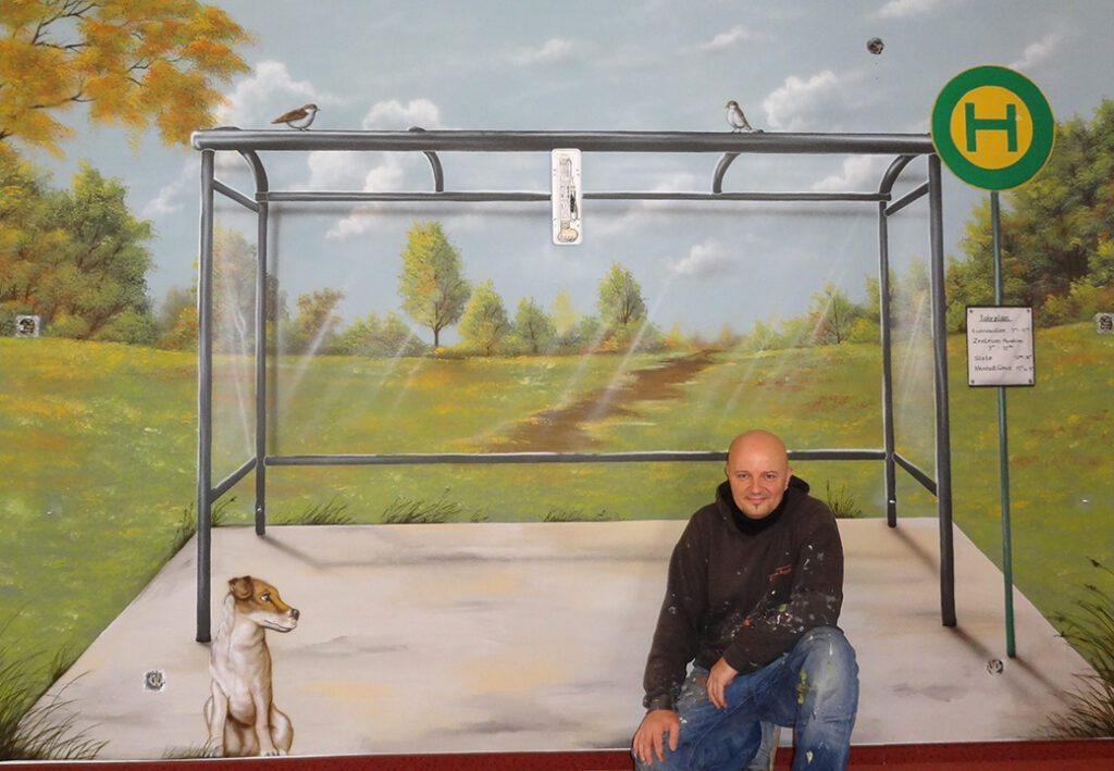 Wandgem&auml;lde eines Buswarteh&auml;uschens mit einem Mann und einem Hund.