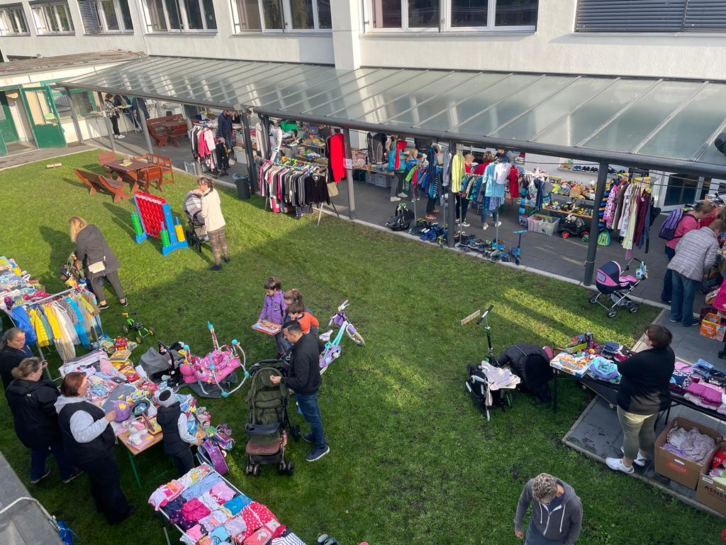 Bildausschnitt eines Flohmarkts, auf dem Menschen an Ständen Kleidung und Spielzeug verkaufen und kaufen