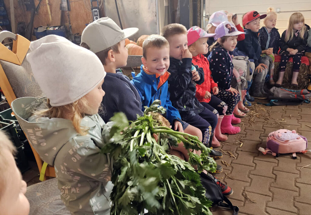 Eine Gruppe von Kindern sitzt in einer Scheune und h&auml;lt Gem&uuml;se.