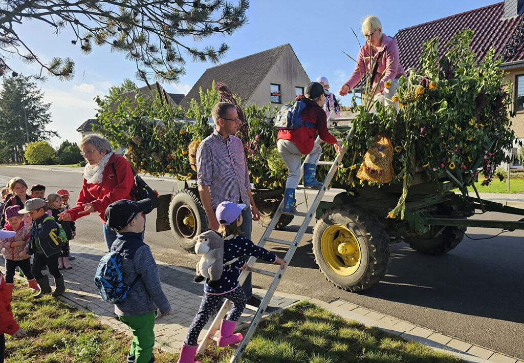 Kinder und Erwachsene besteigen einen geschm&uuml;ckten Traktoranh&auml;nger