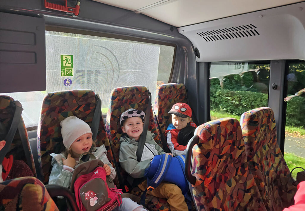 Drei Kinder sitzen in einem Bus und l&auml;cheln.