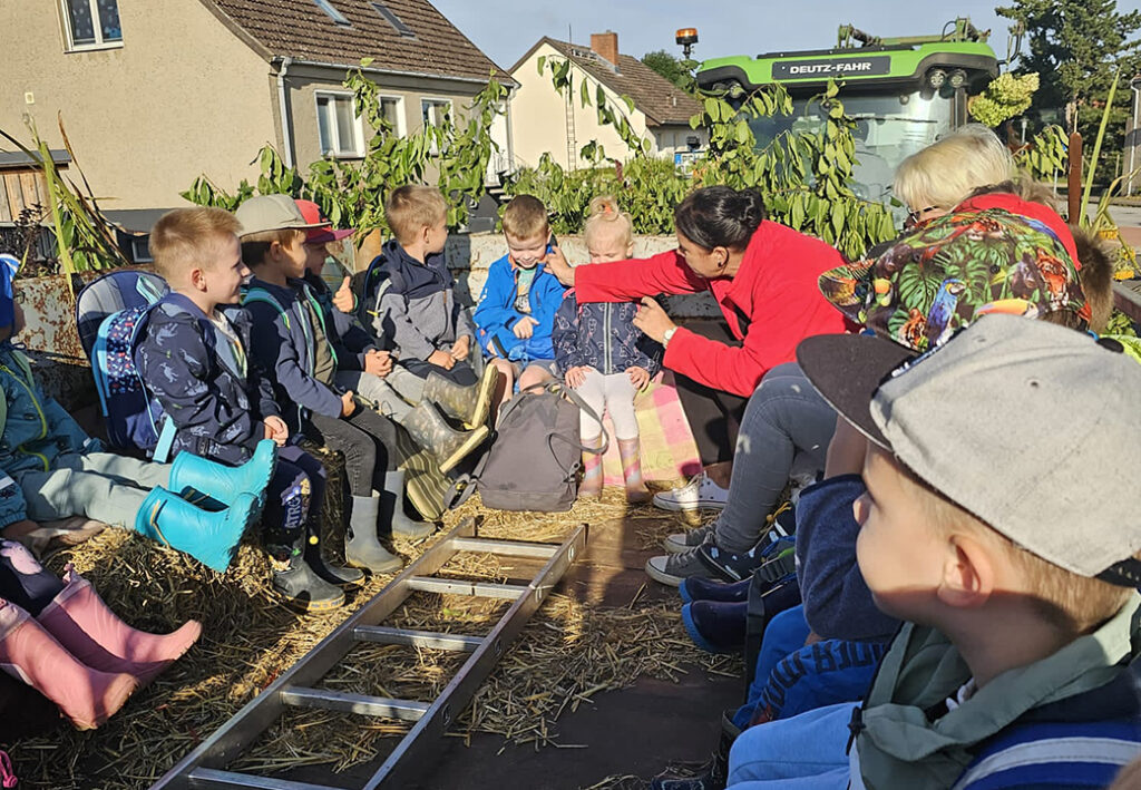 Eine Gruppe von Kindern auf einem Anh&auml;nger, umgeben von Stroh, w&auml;hrend eines Ausflugs.