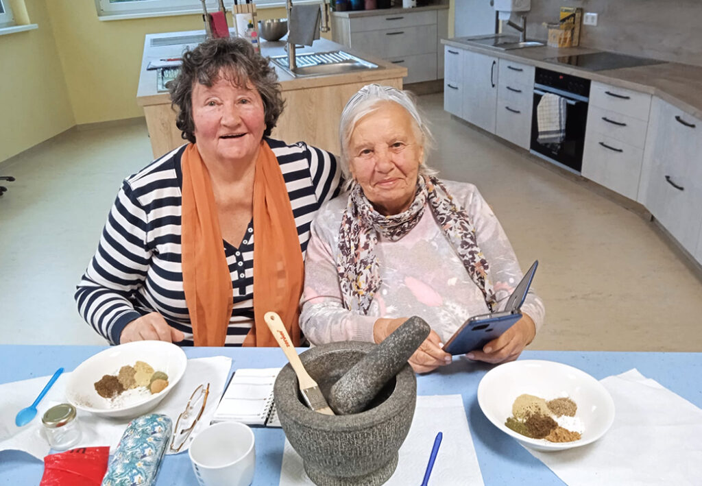 Zwei &auml;ltere Frauen sitzen an einem K&uuml;chentisch.