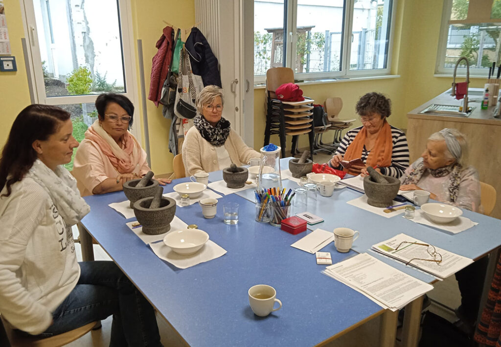 Eine Gruppe von sechs Frauen sitzt um einen Tisch in einem Gemeinschaftsraum.