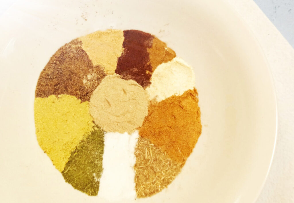 Verschiedenfarbige Gew&uuml;rze in kreisf&ouml;rmigem Muster auf einem Teller angeordnet.