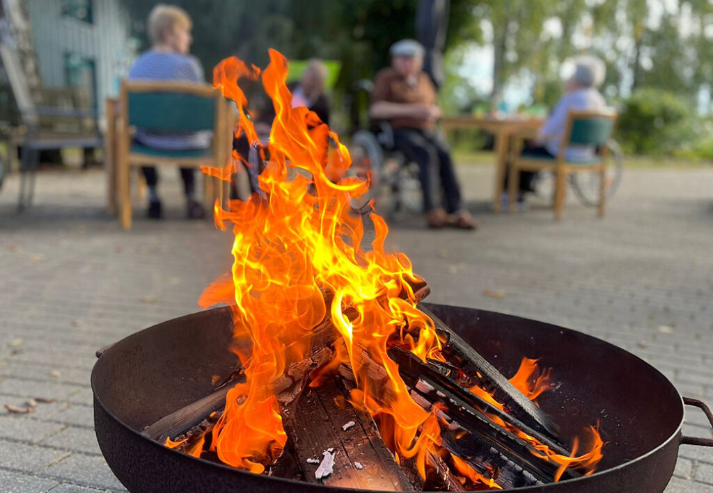 Lagerfeuer im Vordergrund mit Menschen im Hintergrund