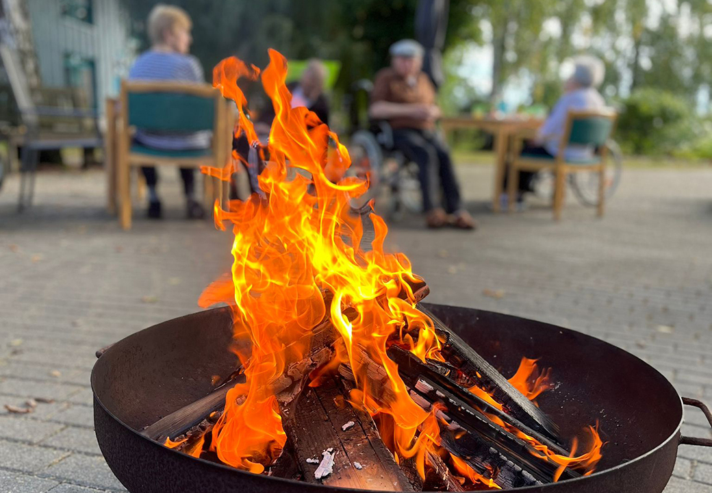 Lagerfeuer im Vordergrund mit Menschen im Hintergrund