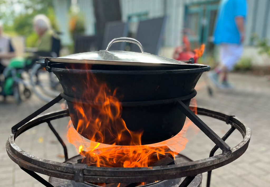 Ein gro&szlig;er schwarzer Kessel auf einem Feuer, im Freien, mit lodernden Flammen unterhalb des Kessels.