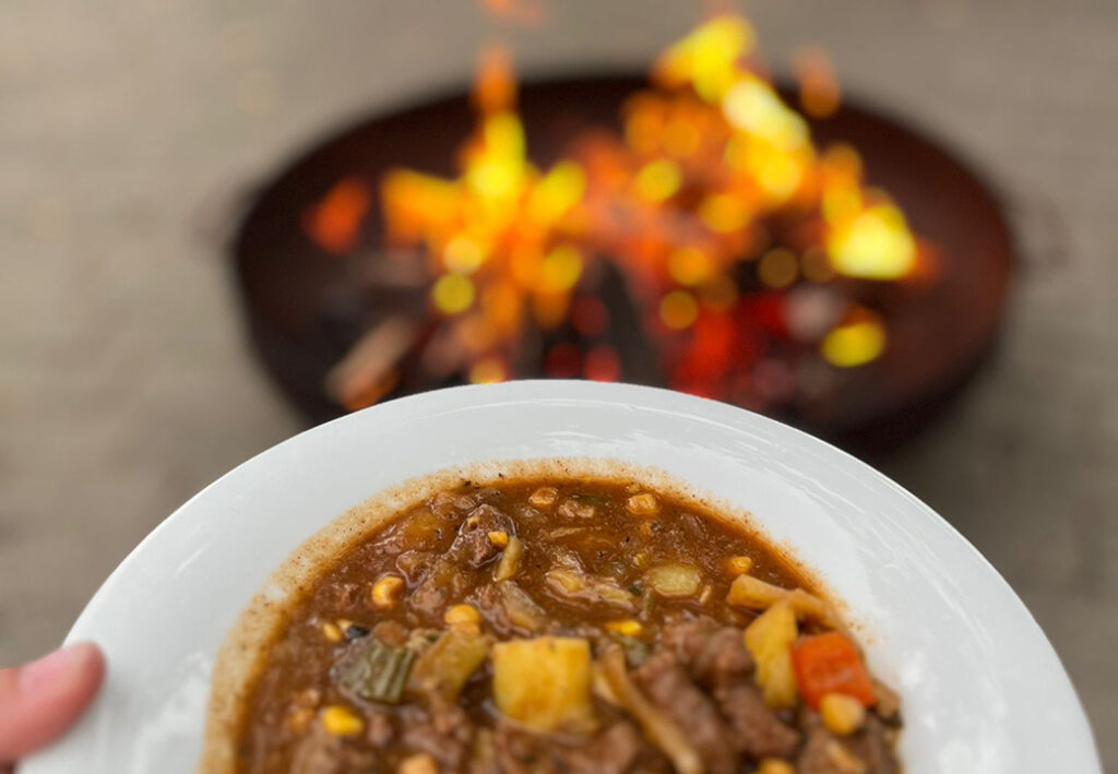 Ein Teller Eintopf vor einem brennenden Lagerfeuer.