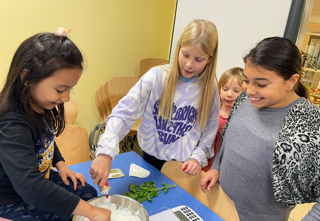 Vier Kinder stehen an einem Tisch mit Kochzutaten.