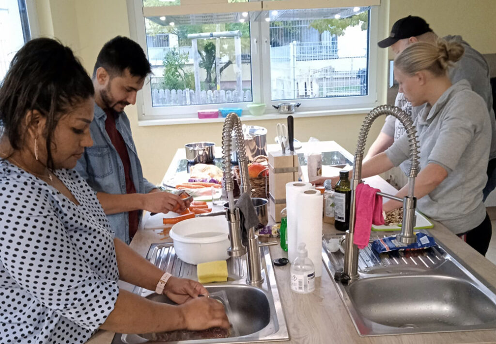 Gruppe von Menschen, die in einer K&uuml;che gemeinsam Gem&uuml;se vorbereiten
