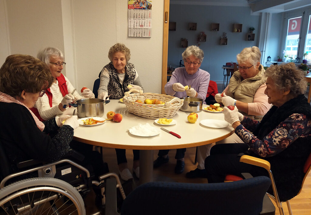 Eine Gruppe älterer Frauen sitzt am Tisch und schält Äpfel.