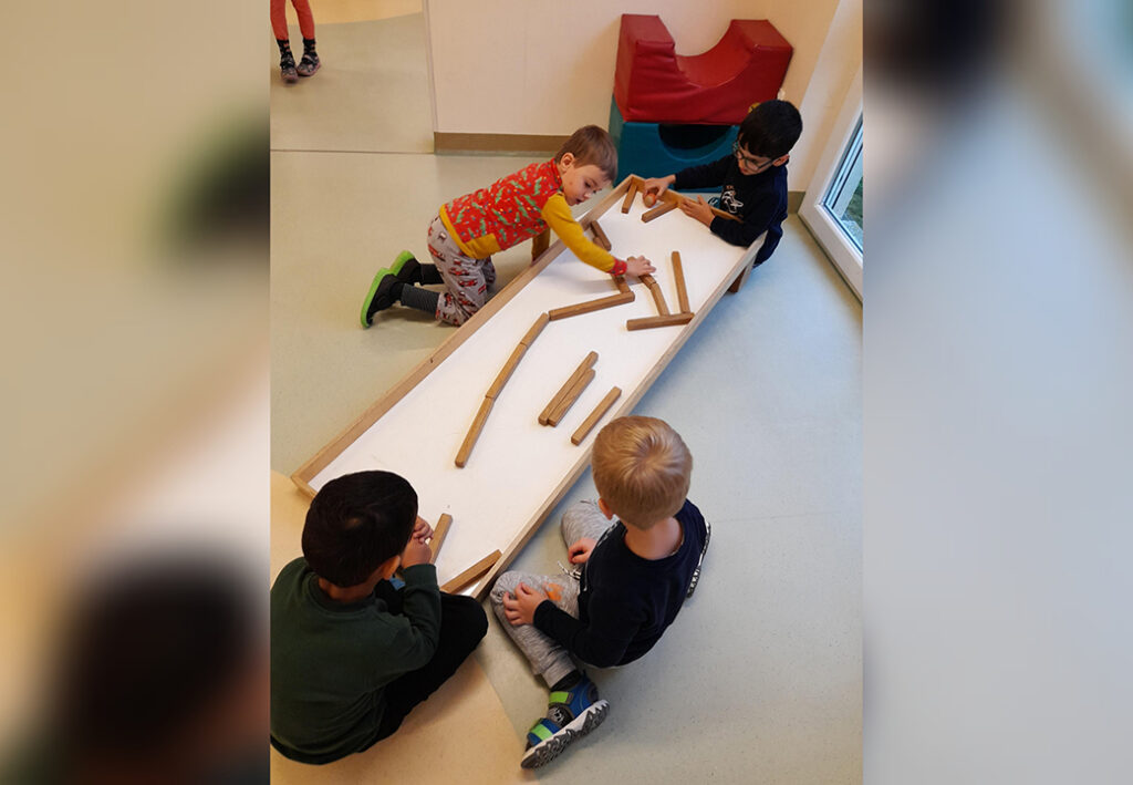 Vier Kinder spielen zusammen mit Holzbausteinen auf einem Tisch.
