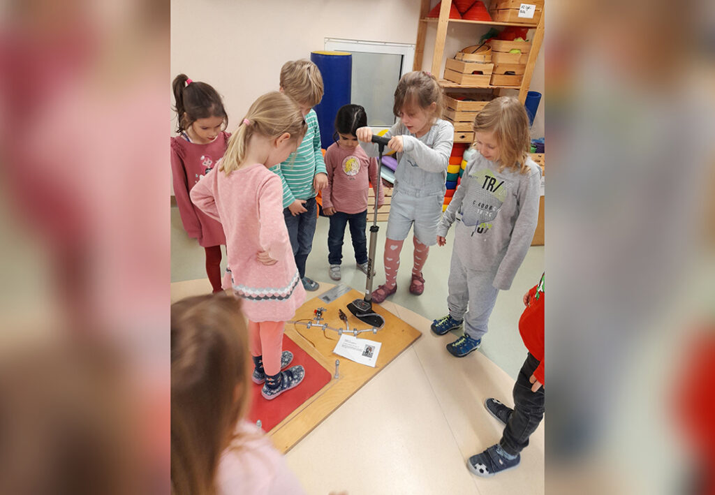 Kinder stehen um eine experimentelle Apparatur und schauen aufmerksam zu