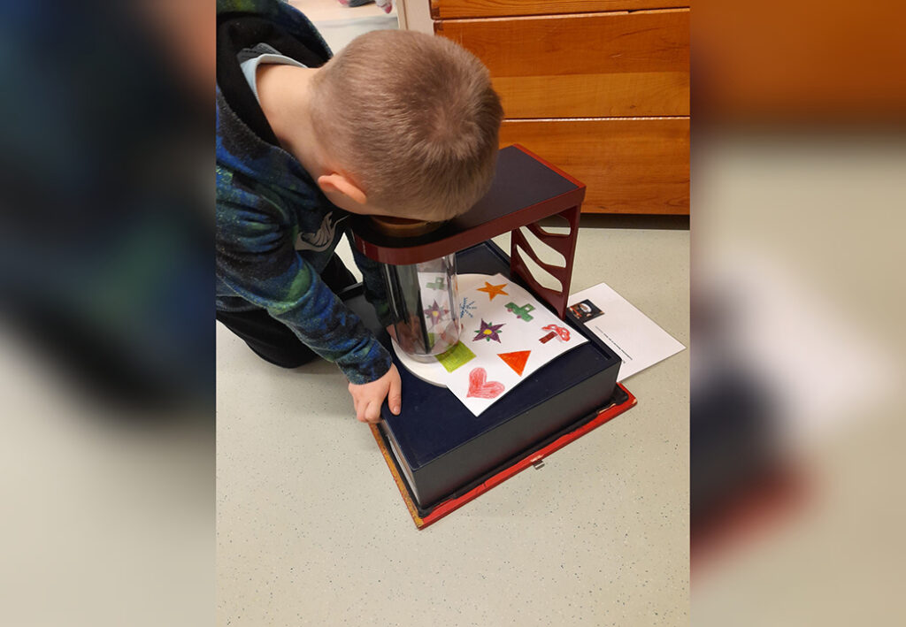 Ein Kind betrachtet ein optisches Ger&auml;t mit bunten Zeichnungen.