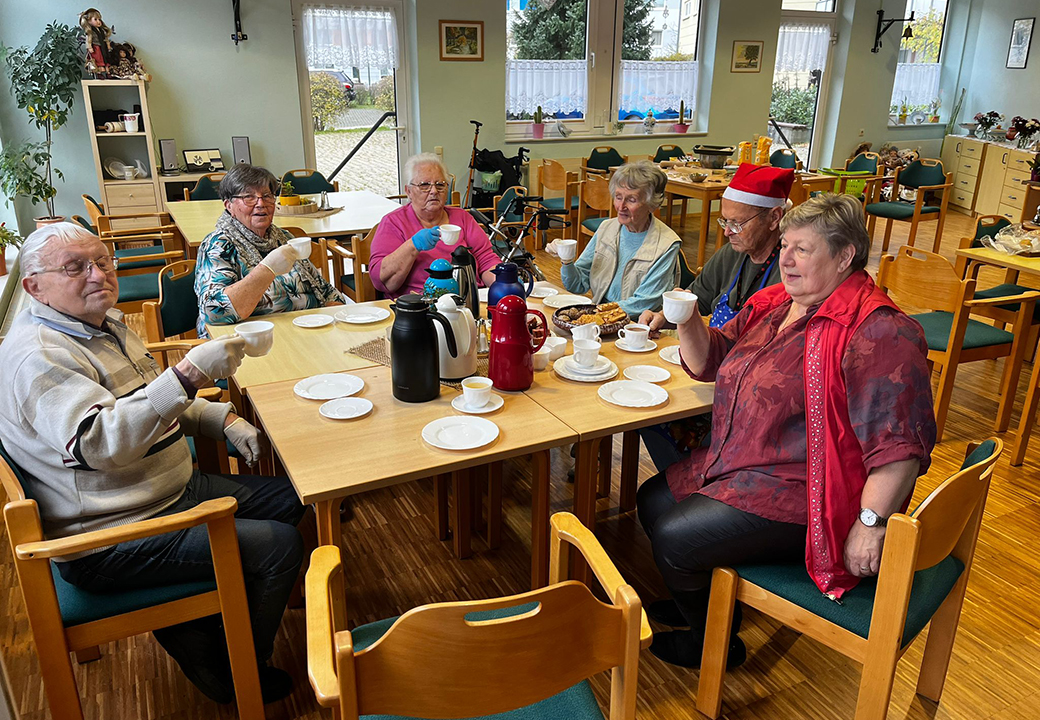 Eine Gruppe älterer Menschen sitzt an einem Tisch und hält Teetassen.