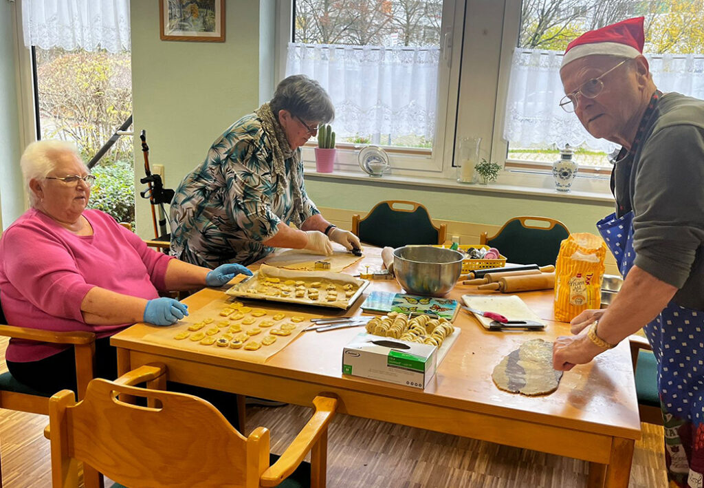 Drei Menschen backen Kekse in einem Raum mit gro&szlig;en Fenstern.