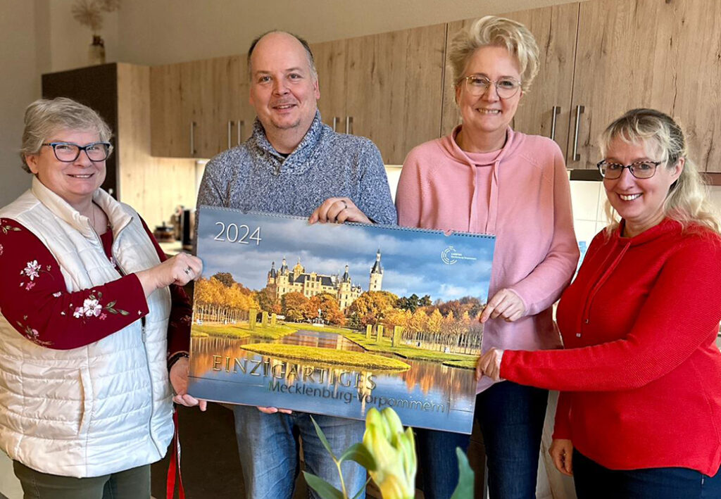 Vier Personen posieren mit einem Kalender mit einem Bild von Mecklenburg Vorpommern.