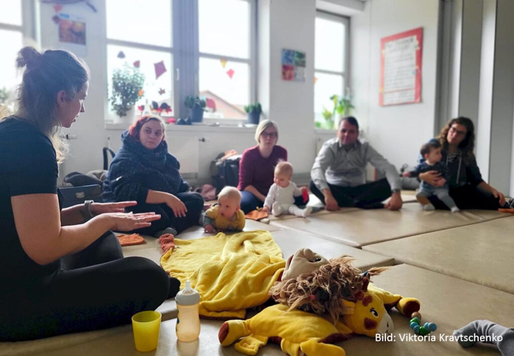 Gruppe von Erwachsenen und Babys in einem Sitzkreis auf dem Boden.
