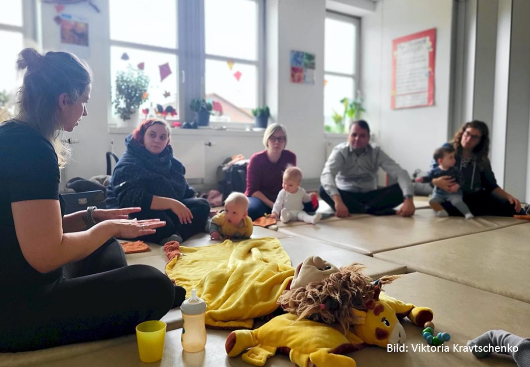 Gruppe von Erwachsenen und Babys in einem Sitzkreis auf dem Boden.