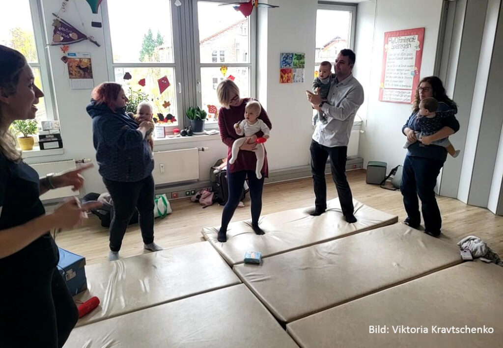 Mehrere Erwachsene halten Babys in einem Raum mit Matten auf dem Boden.