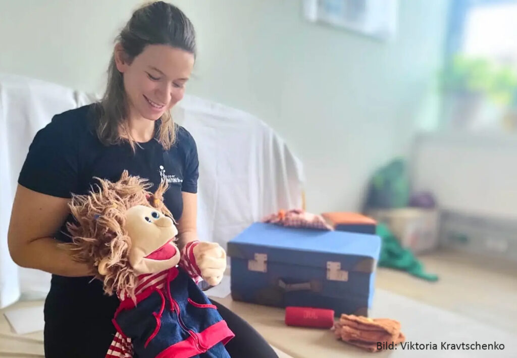 Frau mit Puppentheater-Puppe in einem Raum mit Spielzeug im Hintergrund.