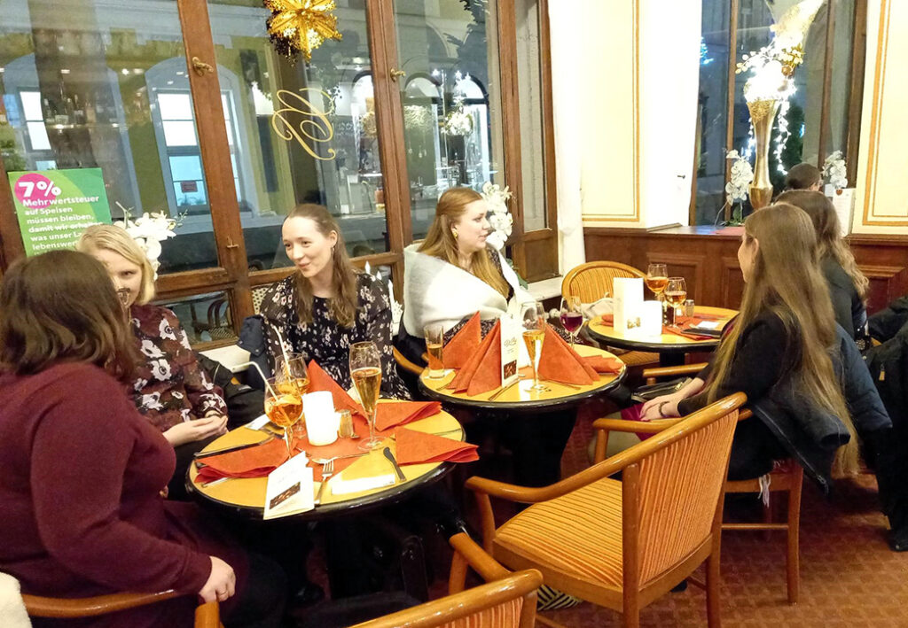 Eine Gruppe von Frauen sitzt an zwei Tischen in einem Café und unterhält sich.