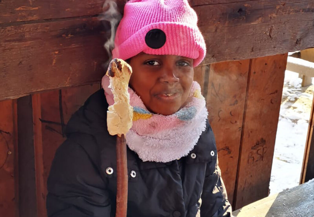 Ein Kind sitzt in warmer Kleidung und h&auml;lt ein Stockbrot.