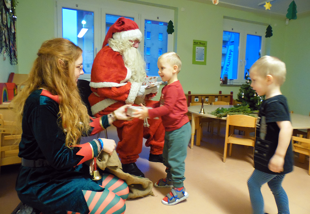 Ein Weihnachtsmann verteilt Geschenke an Kinder in einem Raum.