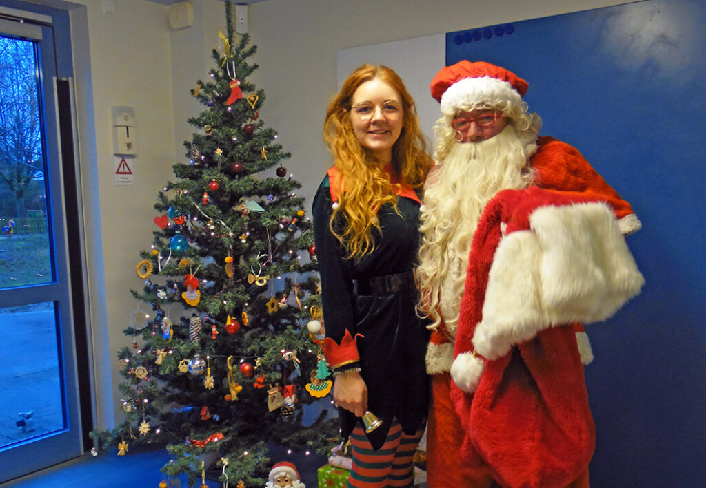 Eine Frau und ein als Weihnachtsmann verkleideter Mann stehen vor einem geschm&uuml;ckten Weihnachtsbaum.