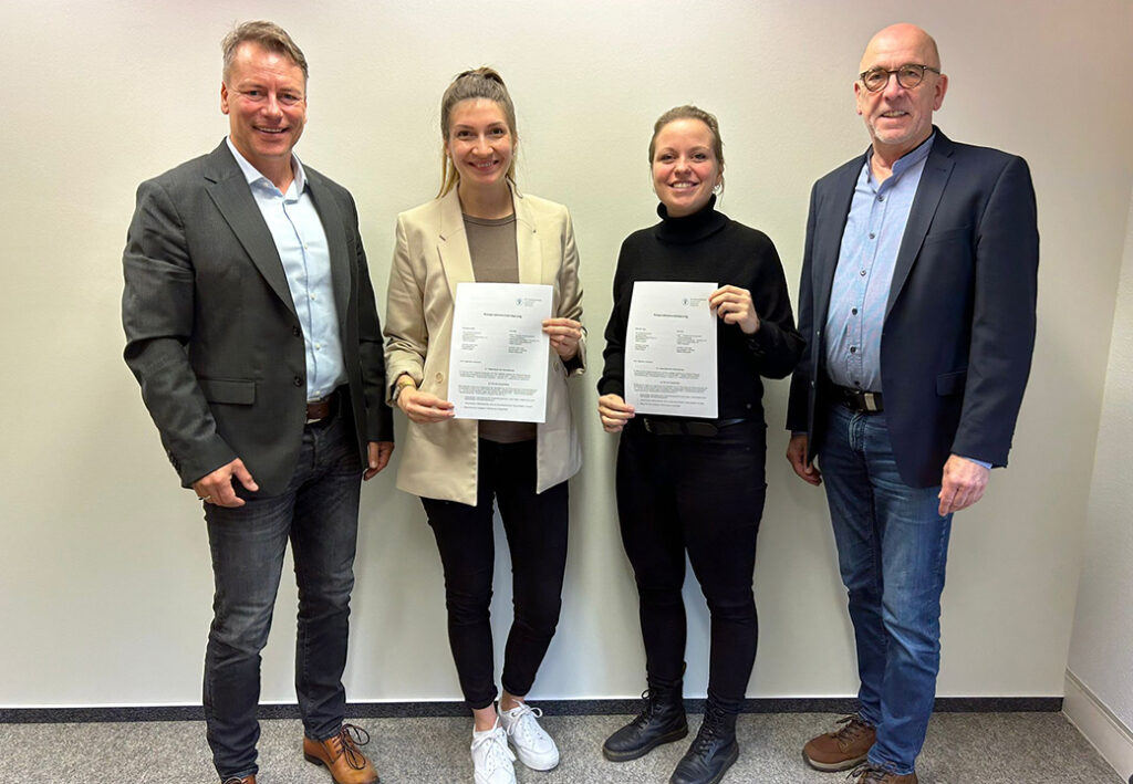 Vier Personen stehen nebeneinander und halten Dokumente.