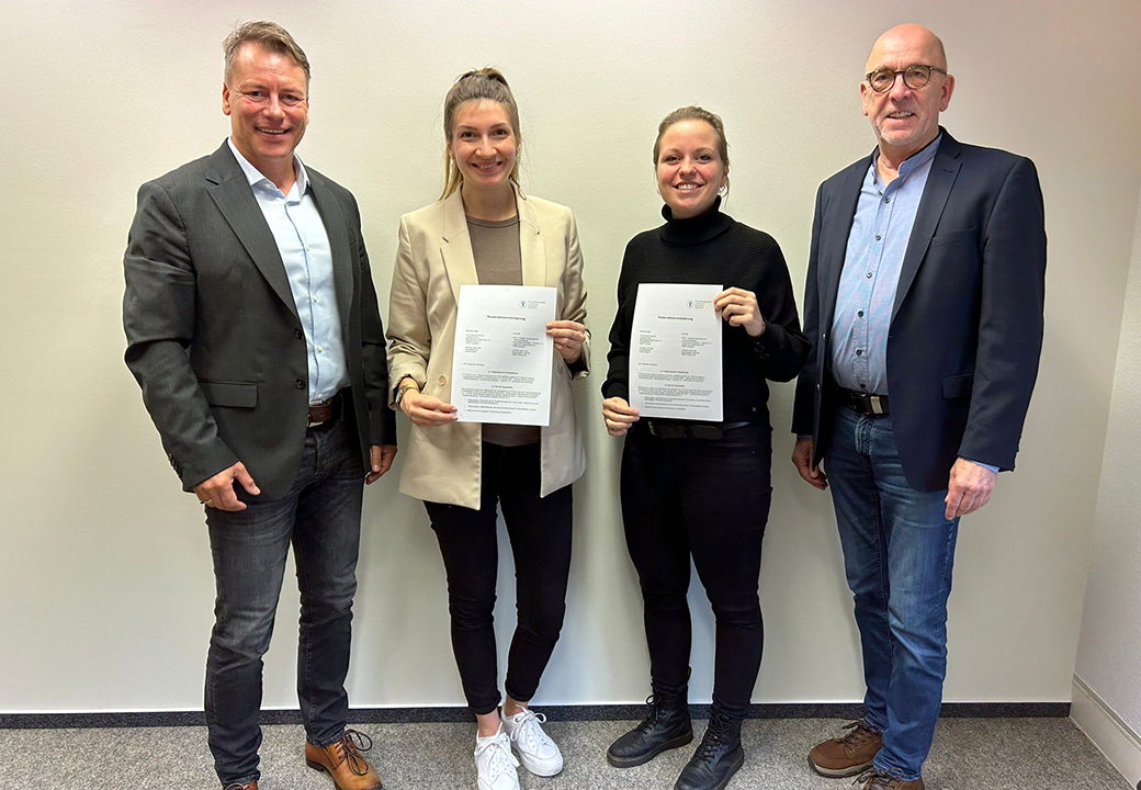 Vier Personen stehen nebeneinander und halten Dokumente.