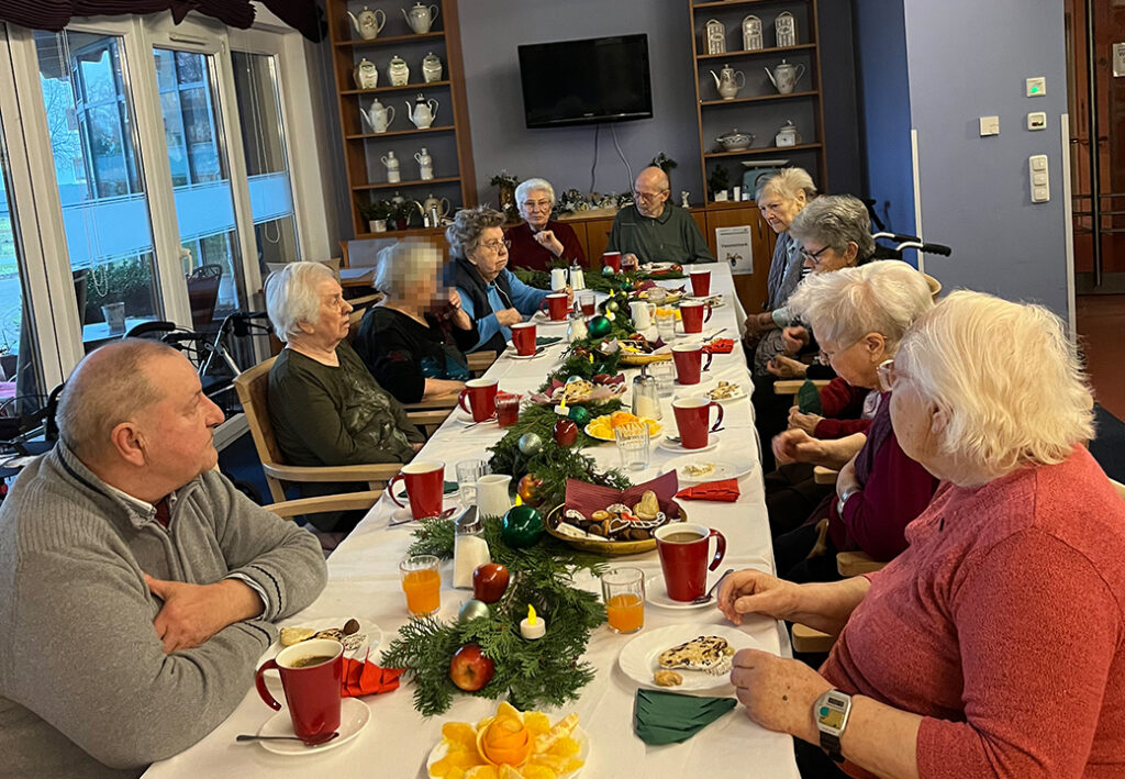 Eine Gruppe &auml;lterer Menschen sitzt an einem festlich gedeckten Tisch in einem Gemeinschaftsraum.
