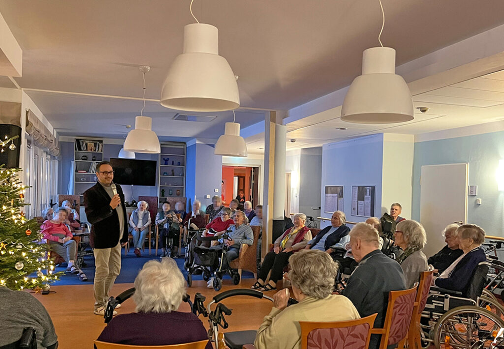 Eine Gruppe von Menschen in einem Gemeinschaftsraum zusammen mit einem Mann, der redet.