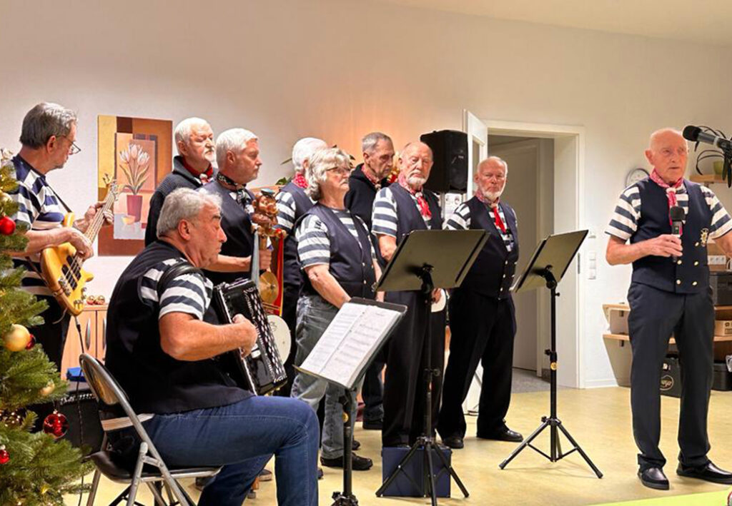 Eine Gruppe &auml;lterer Menschen in gestreiften Hemden und Westen bei einem musikalischen Auftritt.